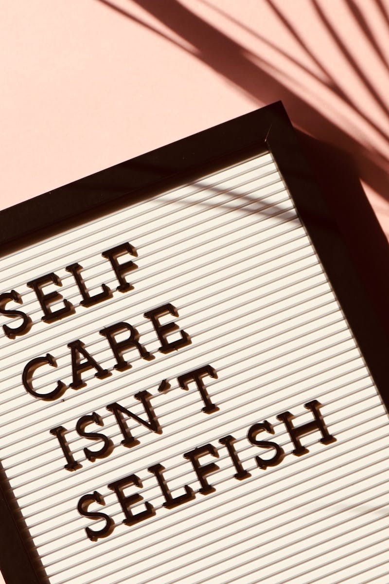 Letter board displaying 'Self Care Isn't Selfish' with artistic shadow on pink background.