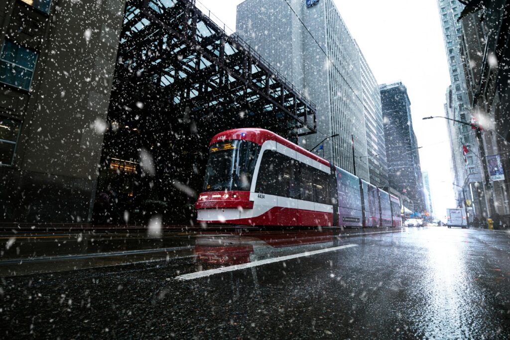A Toronto streetcar navigating a snowy city street during winter with downtown buildings.